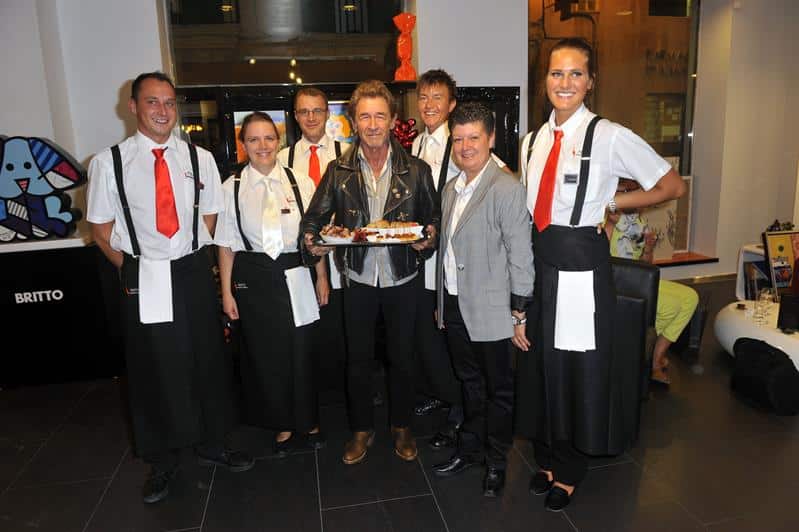 A group of smiling waitstaff in uniforms posing with a man holding a cake in a catering Mallorca restaurant setting.
